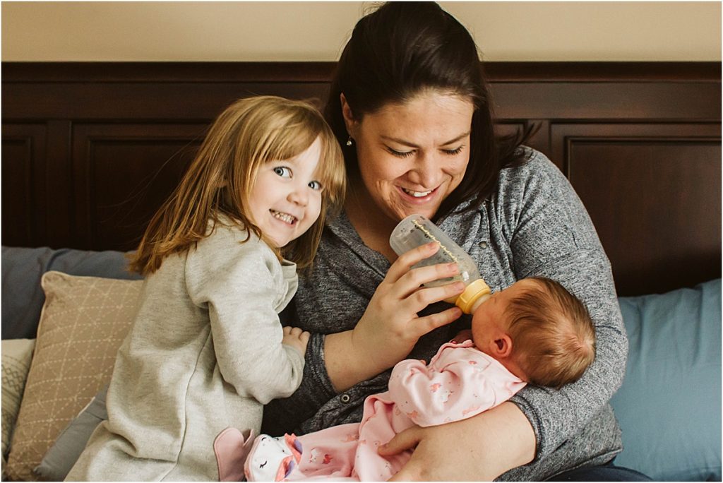 Stephanie feeding her newborn daughter while her older daughter hugs her mother.