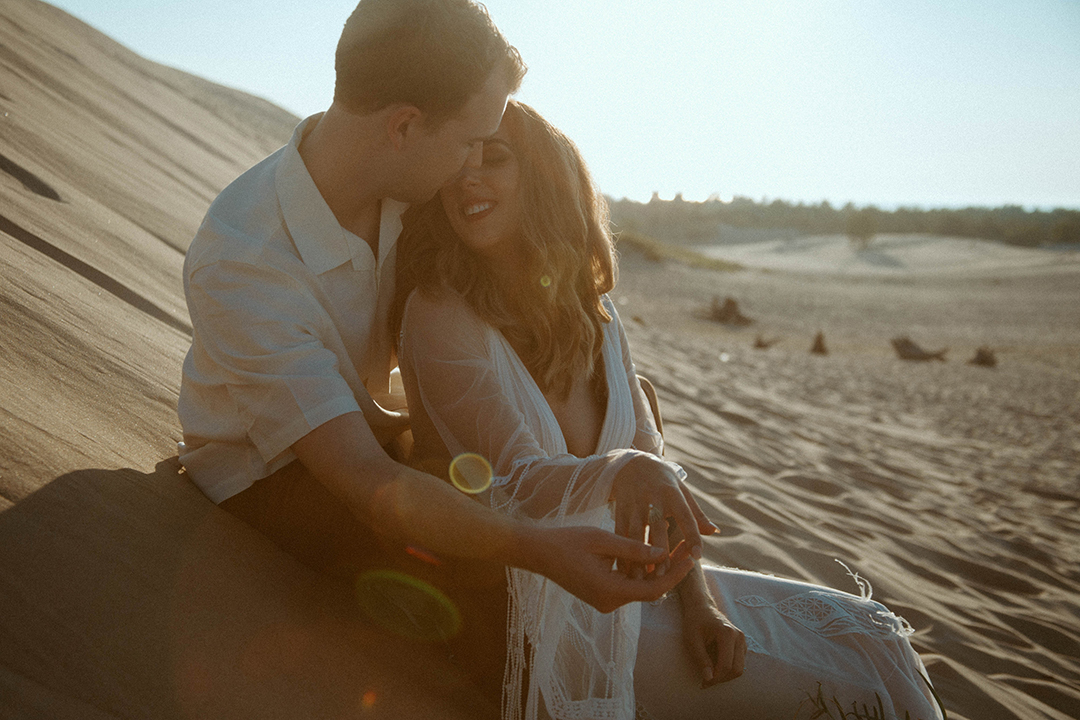 Couple taking bridals at the sand dunes share an intimate moment together at sunset.