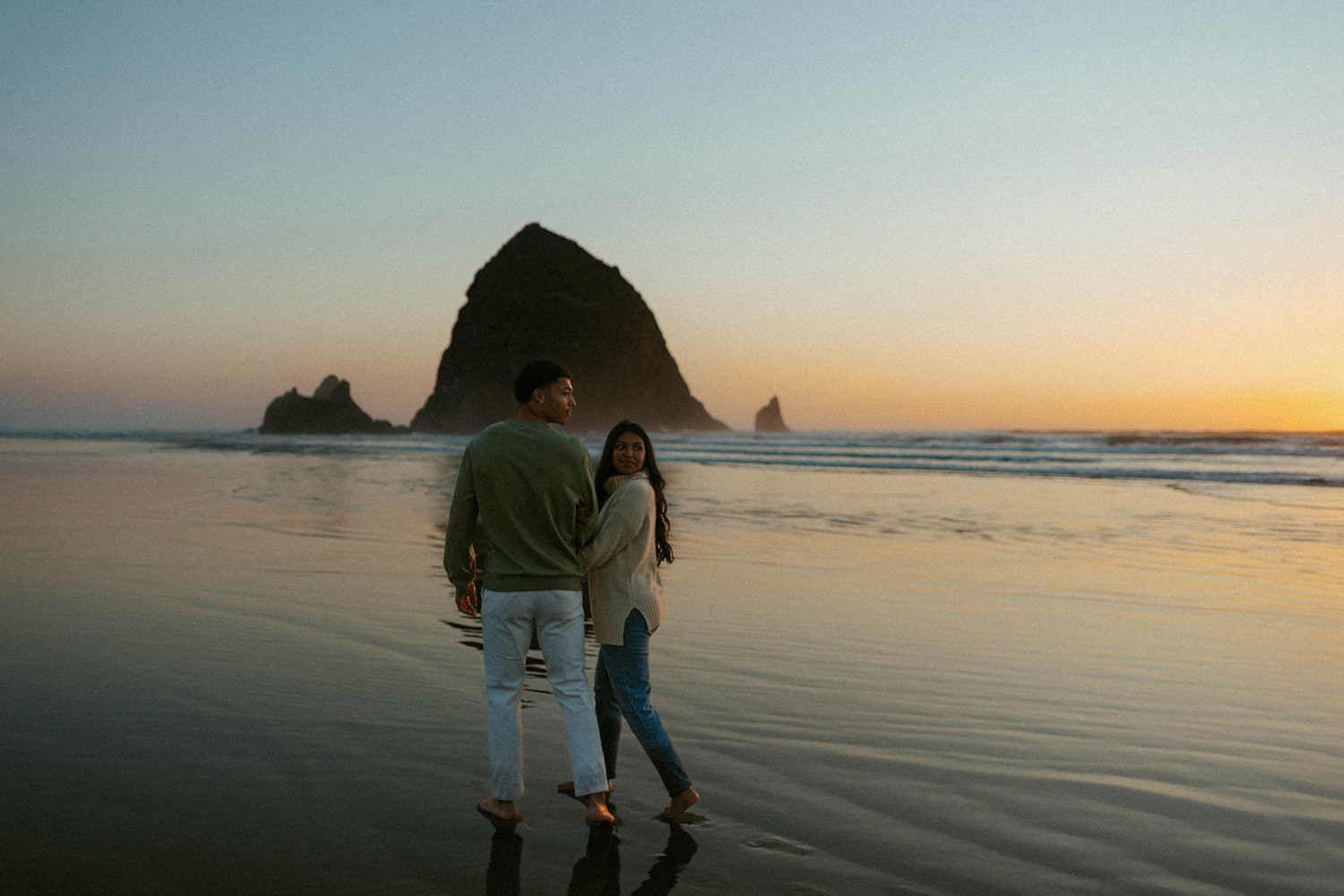 Couple walks together during sunset down Cannon Beach on the Oregon Coast.