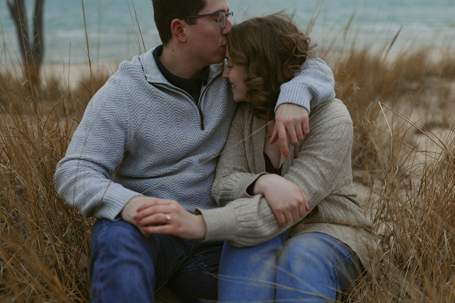 Couple snuggling in the grass together during their lighthouse beach engagement.