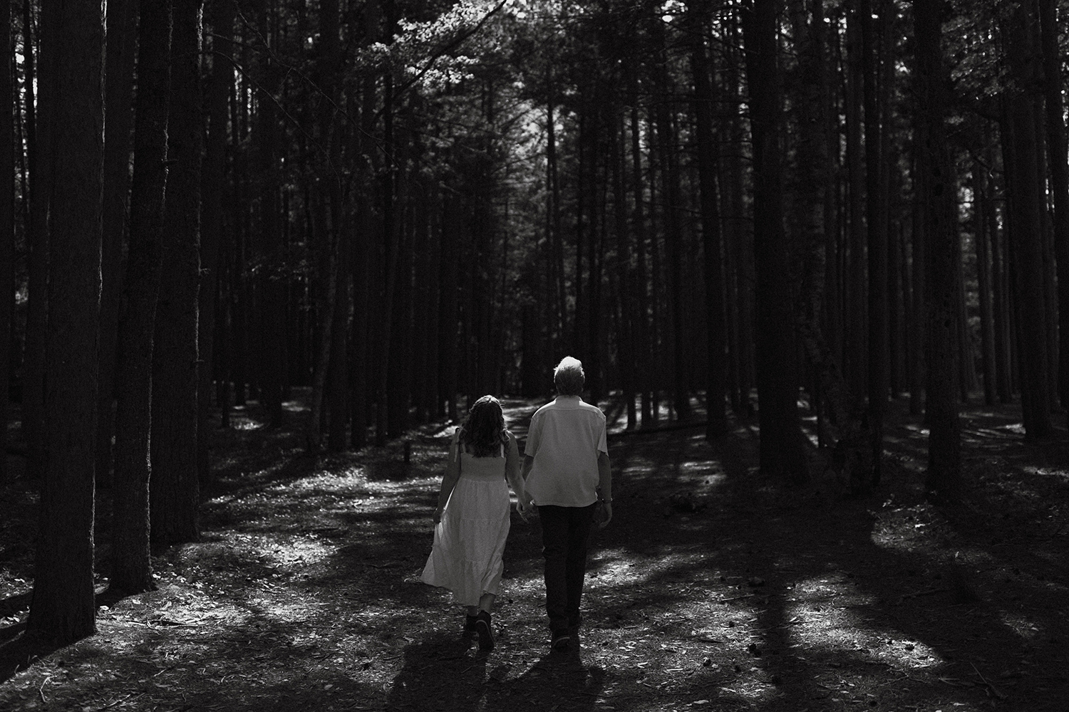 Couple walking under the pines during their engagement session in Marquette.